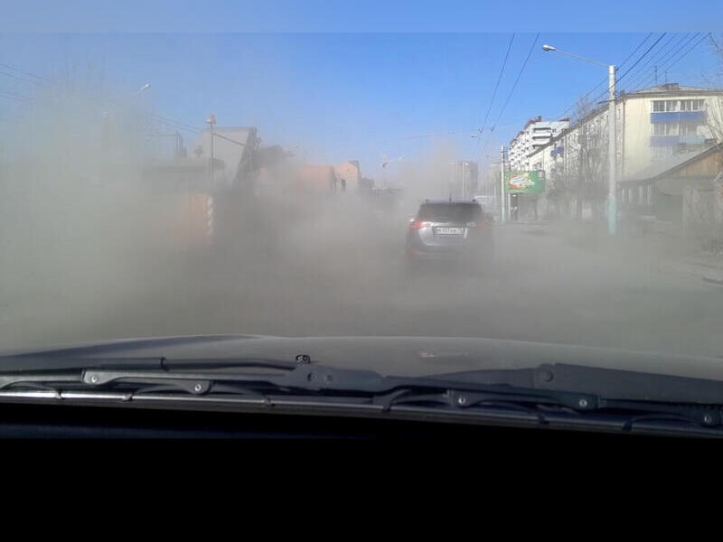 Облака из пыли накрывают машины во время уборки улиц в Чите