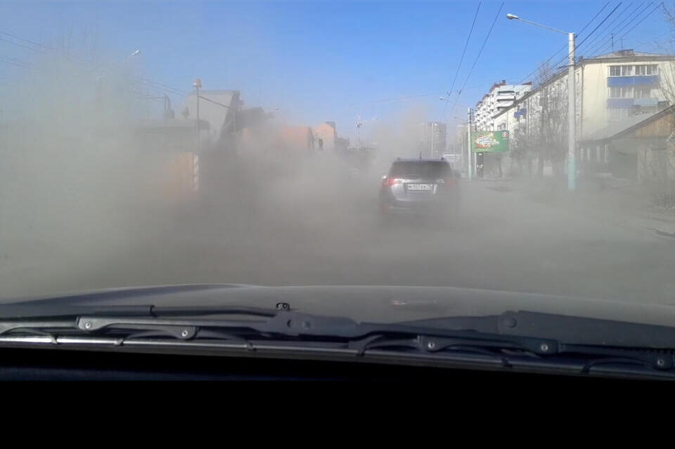 Облака из пыли накрывают машины во время уборки улиц в Чите